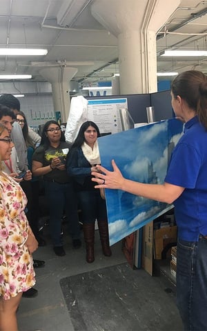 A woman is holding a painting in front of a group of people in a room .
