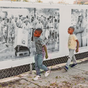 Boys walking in front of a banner tied along a fence