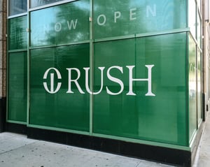 Green window clings with Rush Hospital's logo on a sidewalk corner.
